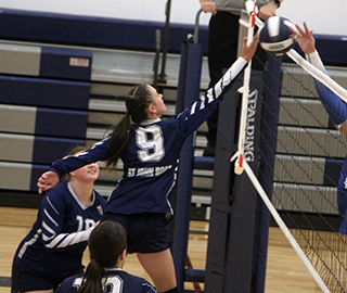 Catherine Beckman battles a Genesee player at the net. Also shown are Miah Mager and Cece Remacle.