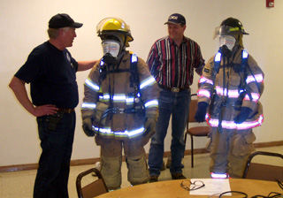 A couple of students dress up in the fire safety equipment. The paper on their facemasks simulates the lack of visibility entering a burning building.