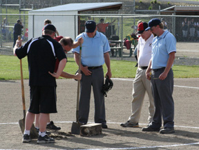 Travis Mader makes the hole bigger for the larger pitching rubber as the umpires and coaches look on. There was a 45 minute delay in the Prairie-Lewis County district game as the rubber was replaced when it was discovered to be too small.