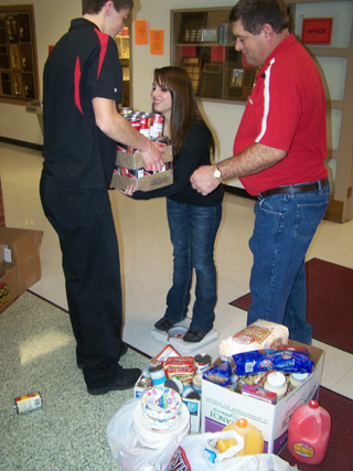 Seth Guyer, Katherine Nida and principal Randy Brown with some of the food donations for the Food Bank at Prairie High School. Katherine stands on the scale so they can get an idea of the number of pounds of food they had donated.