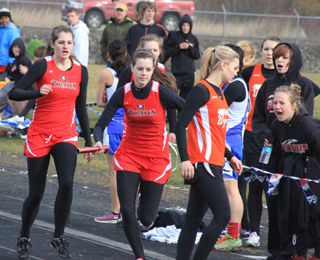 Shelby VonBargen hands off to MaKayla Schaeffer in the 4x400 relay as Brandi Gehring and Abi Chmelik (black sweatshirts at right) scream encouragement. Schaeffer anchored the team to a third place finish.