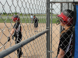 Sarah Seubert looks on from the dugout as Hailey Danly stands in the on deck circle with Steve Wilson as the first base coach. Photo by Kathy Seubert.