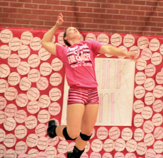 Hailey Danly jump serves against a backdrop of pink volleyballs that represent donations to breast cancer awareness.