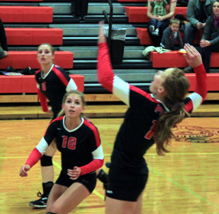 Sarah Seubert spikes the ball at Troy. Also shown are Chaye Uptmor, 10, and Hailey Danly.