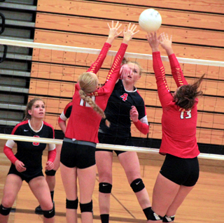 Leah Higgins pounds a spike btween two St. John Endicott blockers as Chaye Uptmor watches.